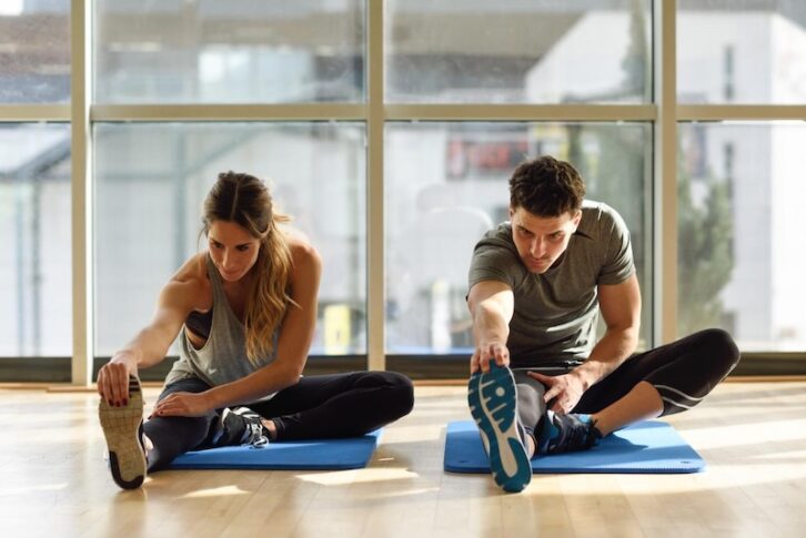 A woman and a man stretching on a yoga mat in a studio. Credit: javi_indy via Freepik
